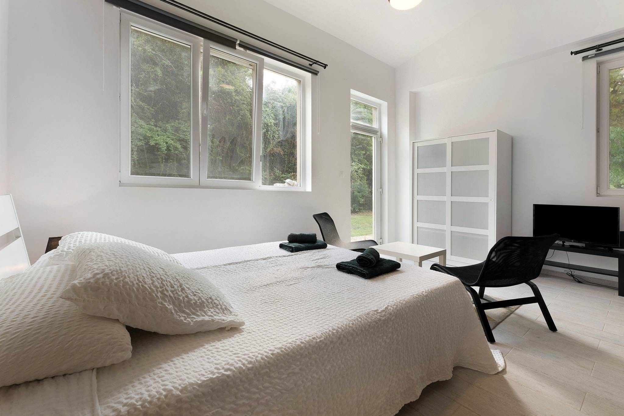 Une chambre moderne avec deux lits, un bureau, une chaise, une armoire et un téléviseur.