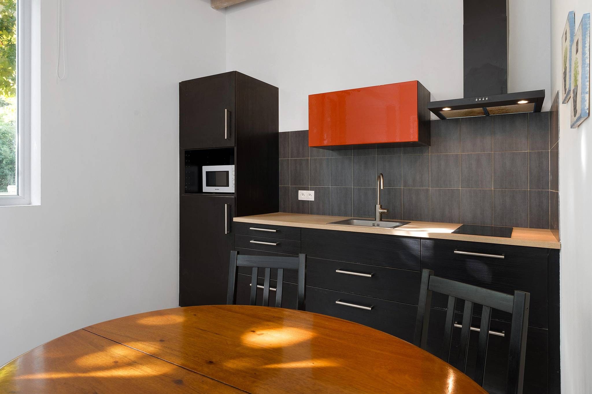 Una cocina moderna con armarios oscuros, una mesa de comedor de madera y una pared de acento roja.