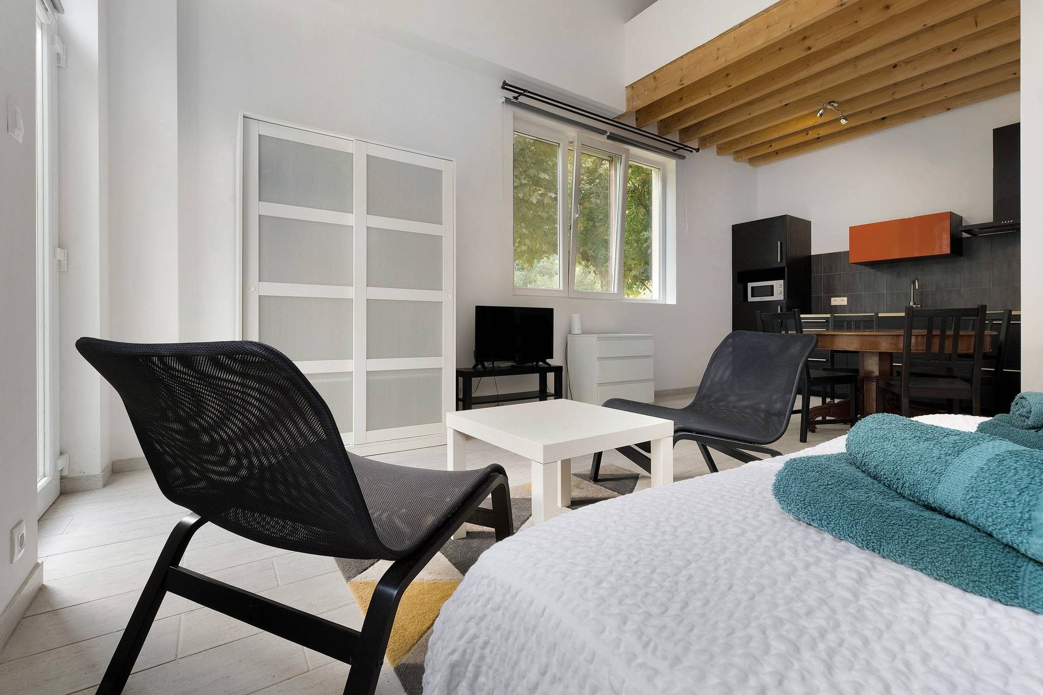 Een moderne kamer met een bed, twee stoelen, een televisie en een eethoek.