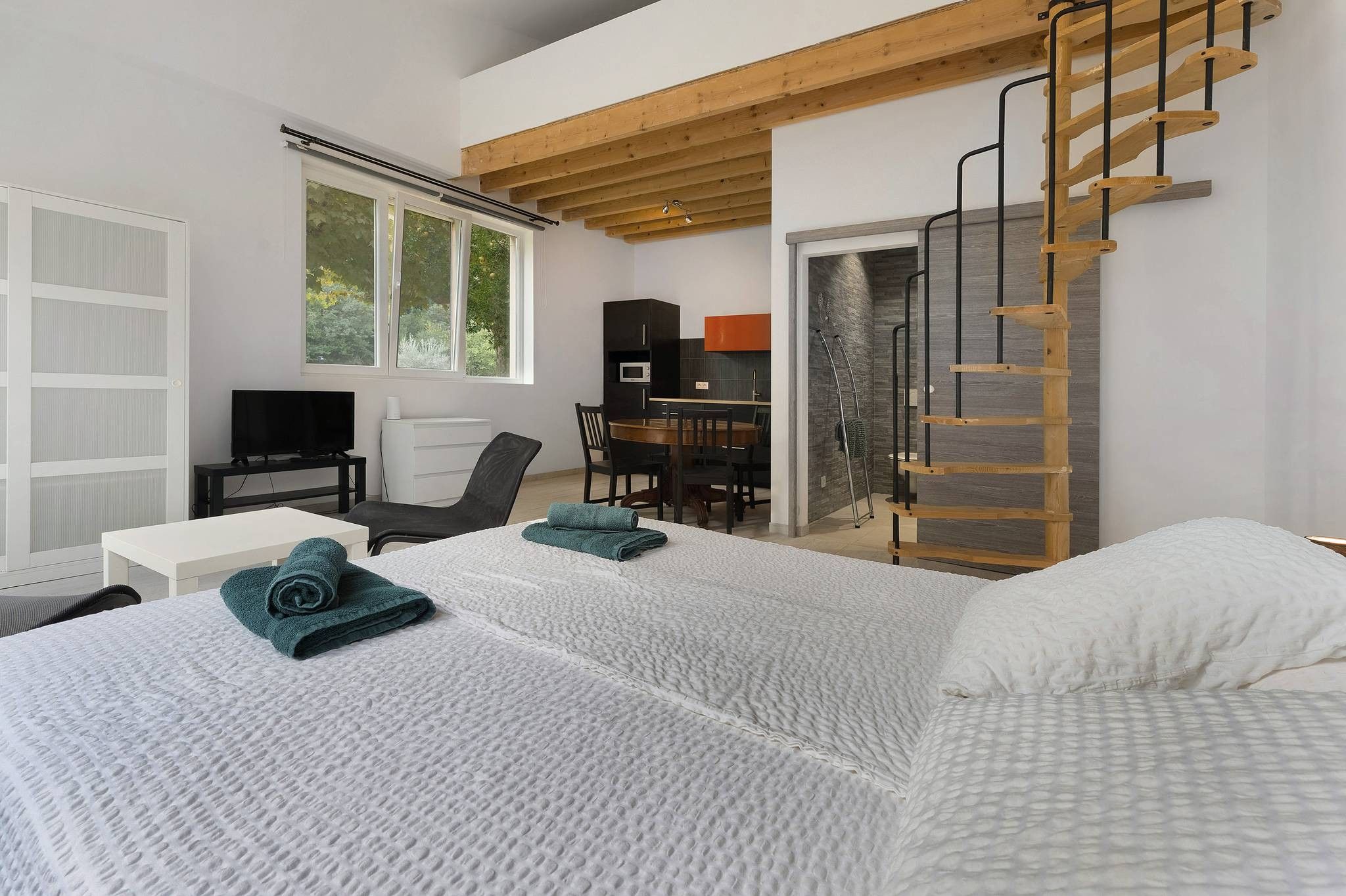 A modern bedroom with two beds, a desk, a chair, and a wooden ladder.