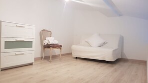 A room with a white dresser, a chair with a brown cushion, and a white sofa. - Charming Studio Le Mas de Kitty, Shared Garden and Pool (Saint-Rémy-de-Provence)