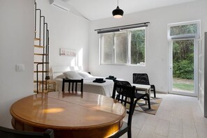 Une chambre moderne avec une table ronde en bois, un lit avec une literie blanche, une chaise noire et une fenêtre donnant sur un paysage verdoyant.