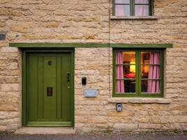 Un edificio de piedra con una puerta verde marcada con el número 6 y una ventana con cortinas rosas.