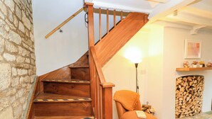 A wooden staircase with a handrail, a chair with a book, a lamp, and a stack of firewood. - Burford Apple (Burford)
