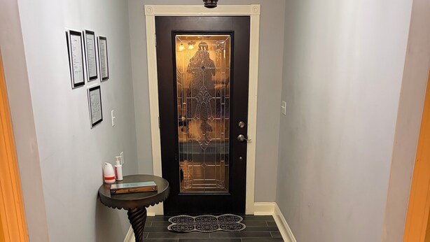 A hallway with a dark wooden floor, a black door with a decorative glass panel, and a small table with a candle and a bottle. - Spacious 3BR/2BA Downtown Eufaula Home Near Lake & Hospital (Eufaula)