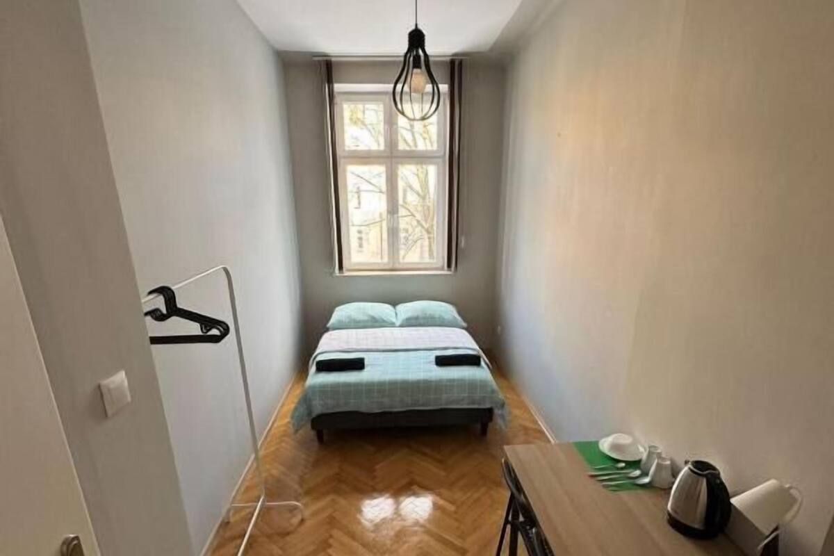 A narrow room with a bed, a table, and a hanging light fixture.