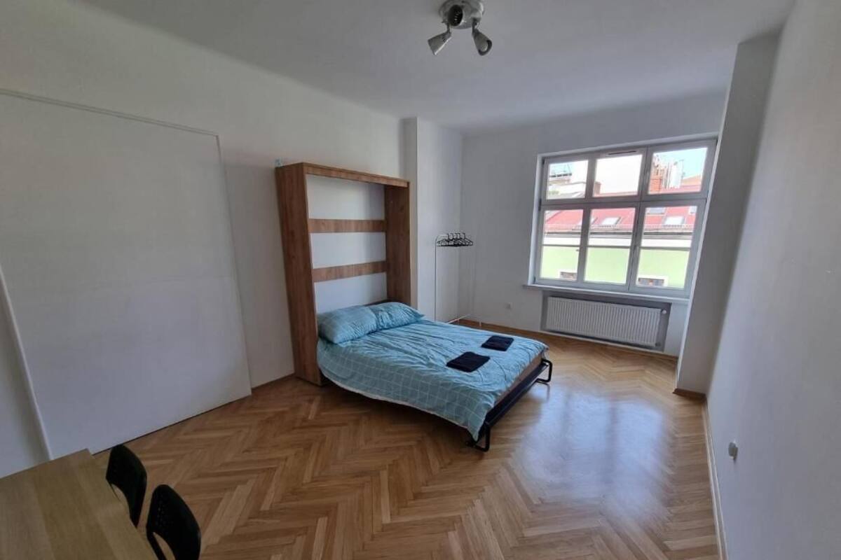 A bedroom with a bed, wooden floor, a window, and a radiator.