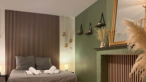 Quarto moderno com cama, abajures, luminária pendente, espelho e painel decorativo na parede.