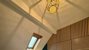 Un lit bien fait, agrémenté de serviettes pliées, une lampe de chevet et un plafond en pente avec une lucarne.