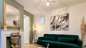 Un salon moderne avec un canapé vert, une table basse blanche, une sculpture en buste et des œuvres d’art abstraites accrochées au mur.