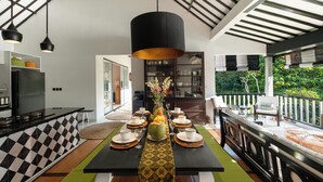 A modern kitchen with a black and white checkered backsplash, a central island with a vase of flowers, and a dining area with a black table set for four. - Bali - Laidback Haven in Ubud with River & Jungle View (Kecamatan Ubud)