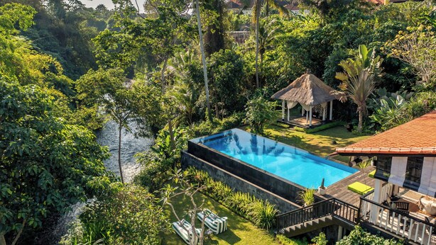 A rectangular swimming pool surrounded by lush greenery, a thatched-roof gazebo, and a wooden deck with outdoor furniture. - Bali - Laidback Haven in Ubud with River & Jungle View (Kecamatan Ubud)