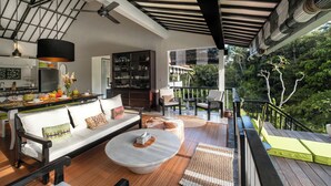 A modern living room with a sofa, coffee table, and chairs, a kitchen area, and a balcony with a view of the surrounding greenery. - Bali - Laidback Haven in Ubud with River & Jungle View (Kecamatan Ubud)