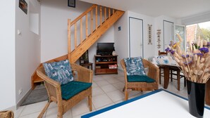 Una sala de estar con muebles de mimbre, una escalera de madera, un televisor y un comedor con mesa y sillas.