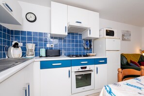 Eine kompakte Küche mit Mikrowelle, Kaffeemaschine und Backofen, eine Uhr sowie eine Couch im angrenzenden Wohnbereich.
