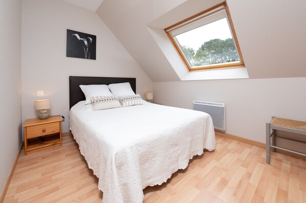 A bedroom with a bed, a nightstand, a lamp, a radiator, a window, and a bench.