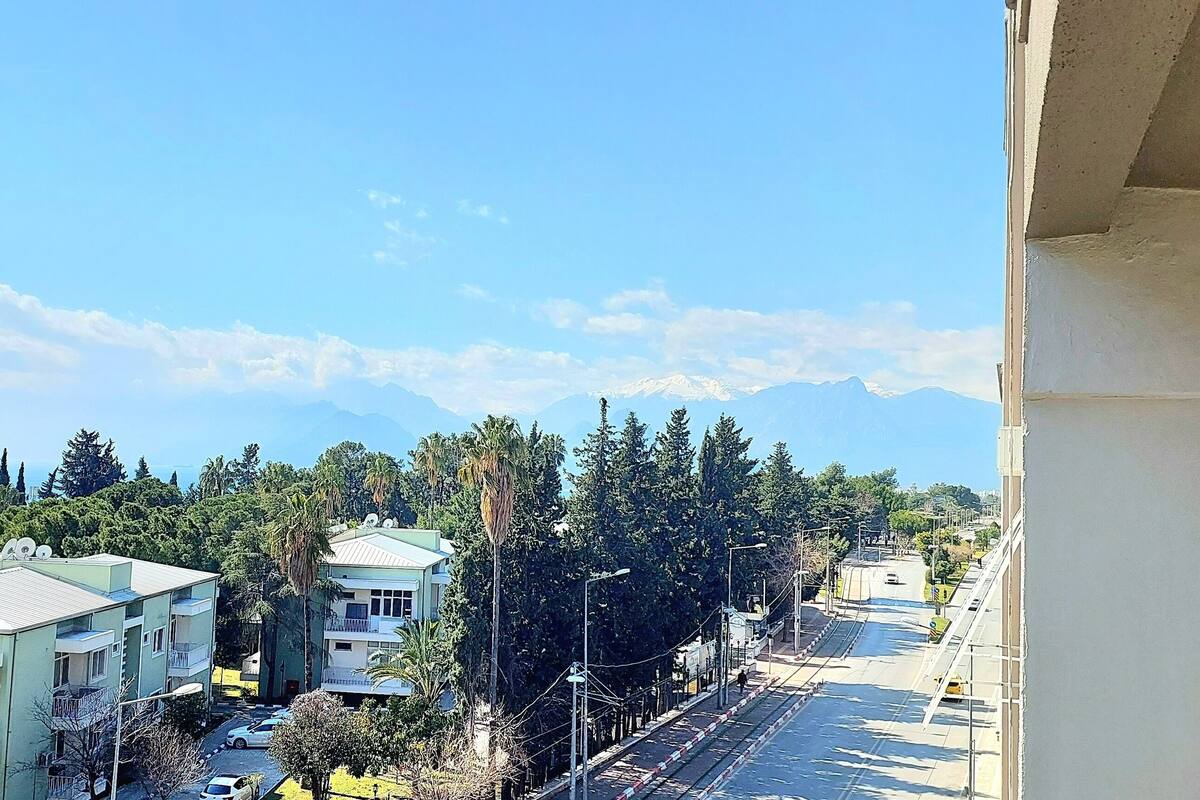 Un quartier résidentiel avec des immeubles à plusieurs étages, un ciel dégagé et une chaîne de montagnes à l’horizon.