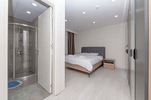 Een moderne slaapkamer met een douchecabine van glas, een bed met witte lakens en een nachtkastje.