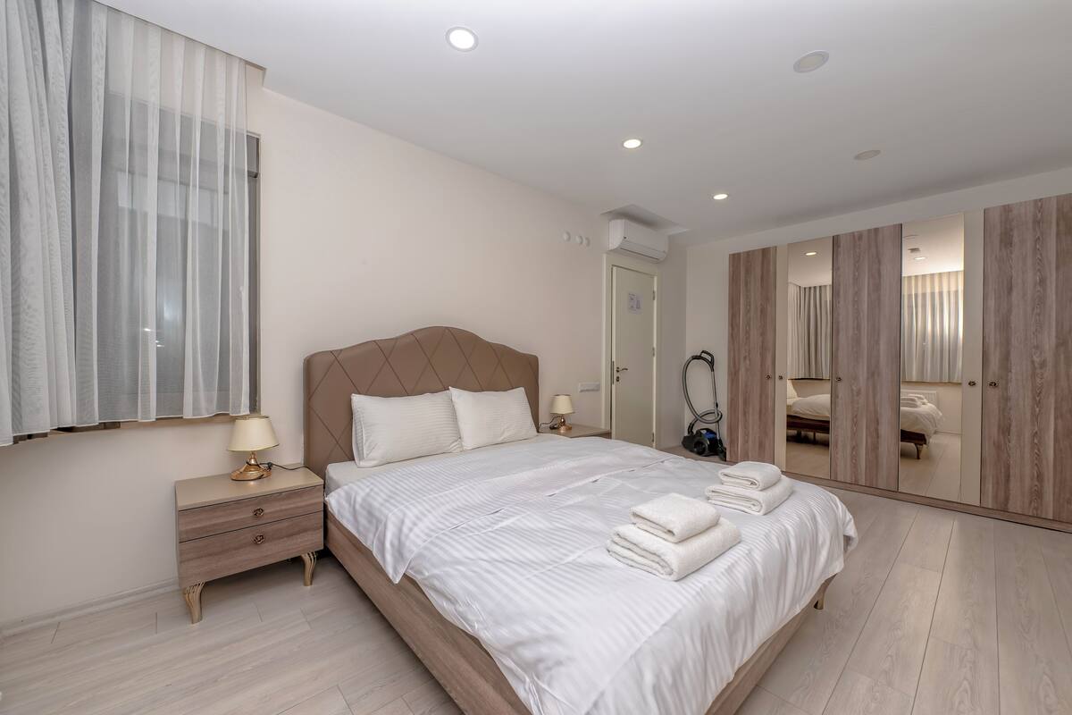 Une chambre à coucher comprenant un lit, une table de chevet, un miroir, une armoire et une fenêtre avec des rideaux.