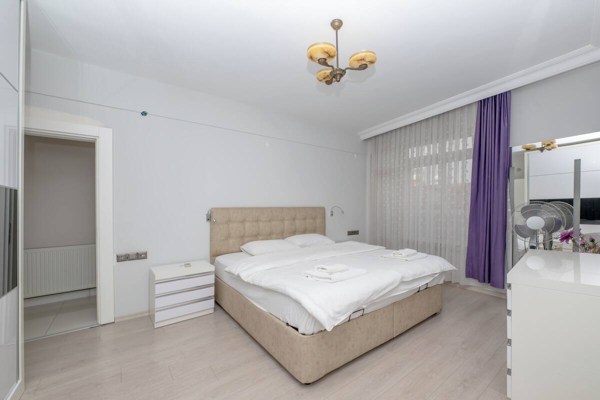 Une chambre moderne avec un lit, des tables de chevet, une armoire, un ventilateur de plafond et une fenêtre avec des rideaux.