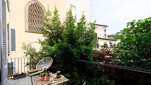 Un balcón con una mesa de madera, sillas y macetas.