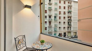 Un balcon avec une petite table et une chaise, un pot de fleurs et une vue sur un immeuble à plusieurs étages doté de balcons.