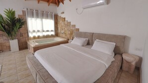 A bedroom with a large bed, a stone wall, a bathtub, and a potted plant.