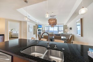 A modern kitchen with a black granite countertop, stainless steel sink, and pendant lighting. - Turquoise Place 1606D by Liquid Life (Orange Beach)