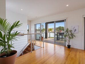 A spacious room with a wooden floor, a staircase with metal railings, a balcony with a view of the water, and a potted plant. - Baravi Breeze Retreat (Safety Beach)