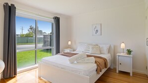 A bedroom with a large window, a bed with white bedding, two bedside tables with lamps, and a wall-mounted artwork. - Baravi Breeze Retreat (Safety Beach)