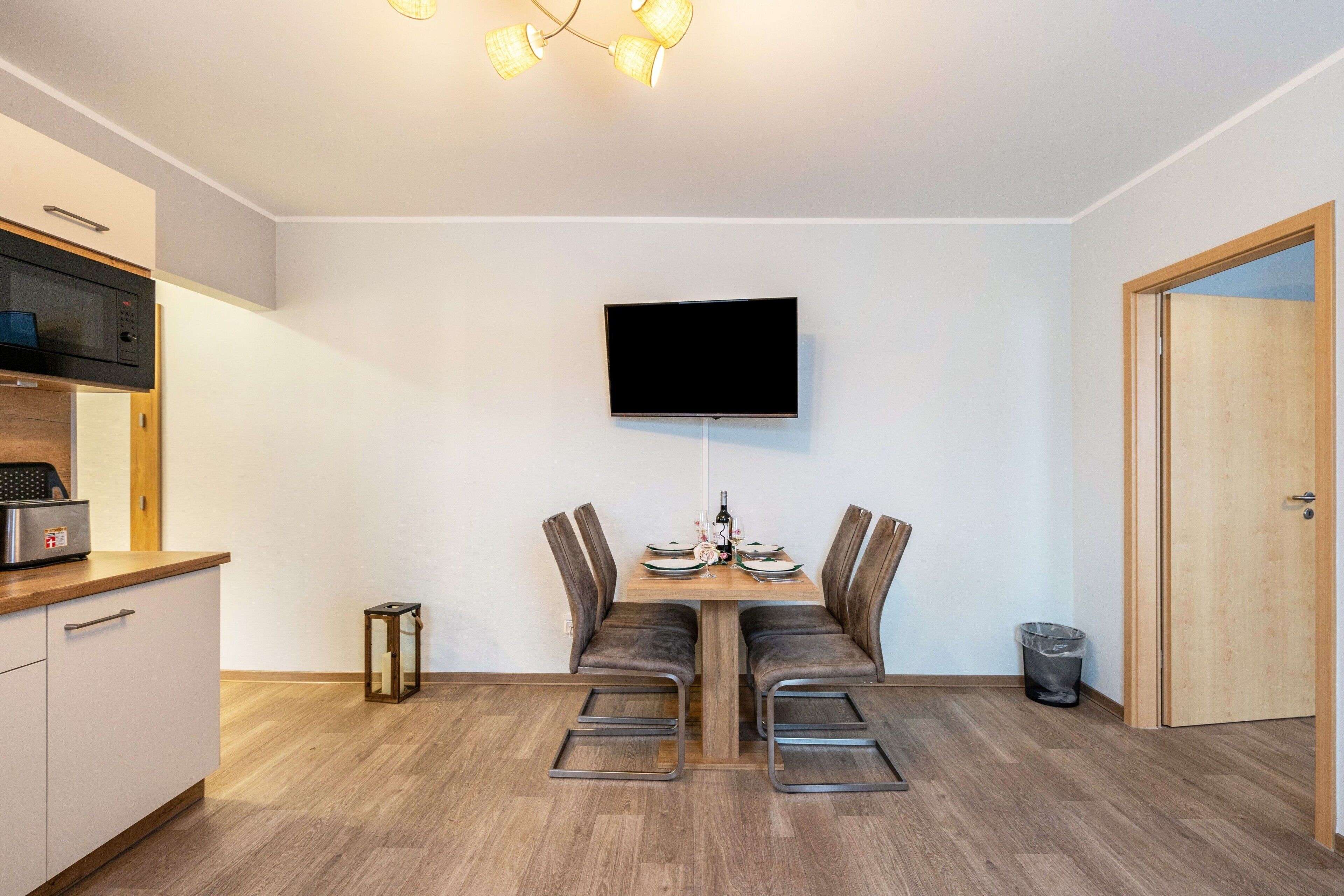 Eine moderne Küche mit Mikrowelle, einem Esstisch mit Stühlen, einem an der Wand montierten Fernseher und einer Holztür.