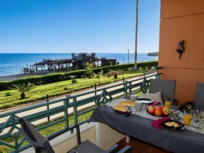 A balcony table with breakfast items, a view of the sea, and a building with a castle-like structure in the background. - Apartment 'Tesoro Del Mar' with Sea View, Wi-Fi, and Air Conditioning (Torrox Costa)