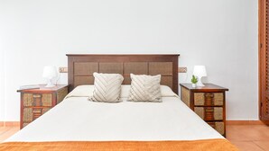A neatly made bed with a wooden headboard, two bedside tables with lamps, and a woven nightstand.