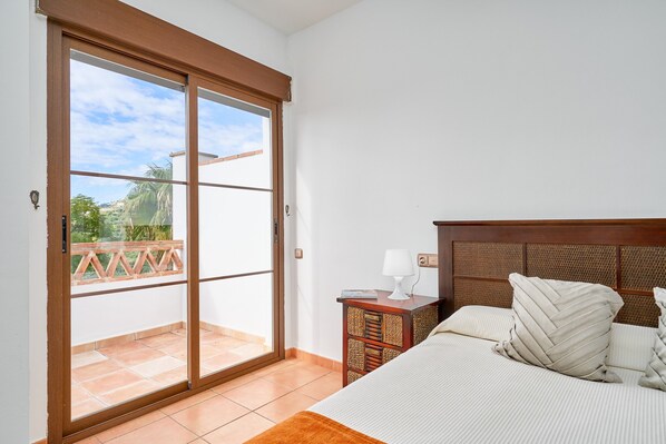 A bedroom with a bed, a nightstand, a lamp, and a sliding glass door leading to a balcony.
