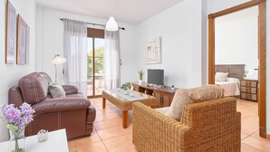 A furnished living room with a sofa, armchair, table, TV, and a view of the outdoors.