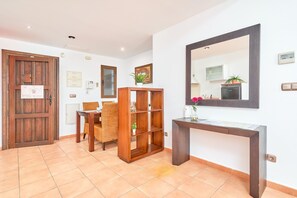 Una habitación con puerta de madera, una mesa de comedor con sillas, una estantería de madera, una consola con espejo y una planta en maceta.