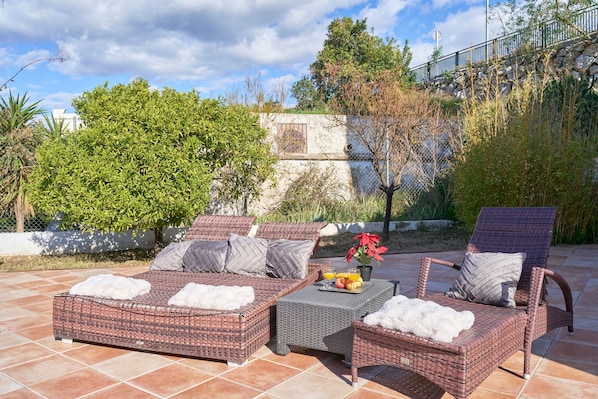 A patio with wicker furniture, a table with fruit, and a potted plant.