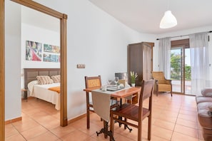 A room with a bed, a dining table with chairs, a sofa, a cabinet, and a balcony with curtains.