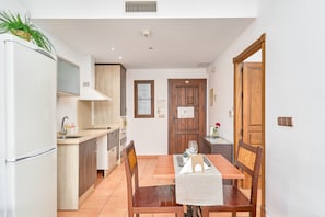 A compact kitchen with a dining area, white walls, wooden cabinets, and a central door.