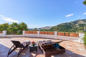 Terraço no telhado com móveis de vime, uma mesa com um vaso e vista para a cidade e colinas.