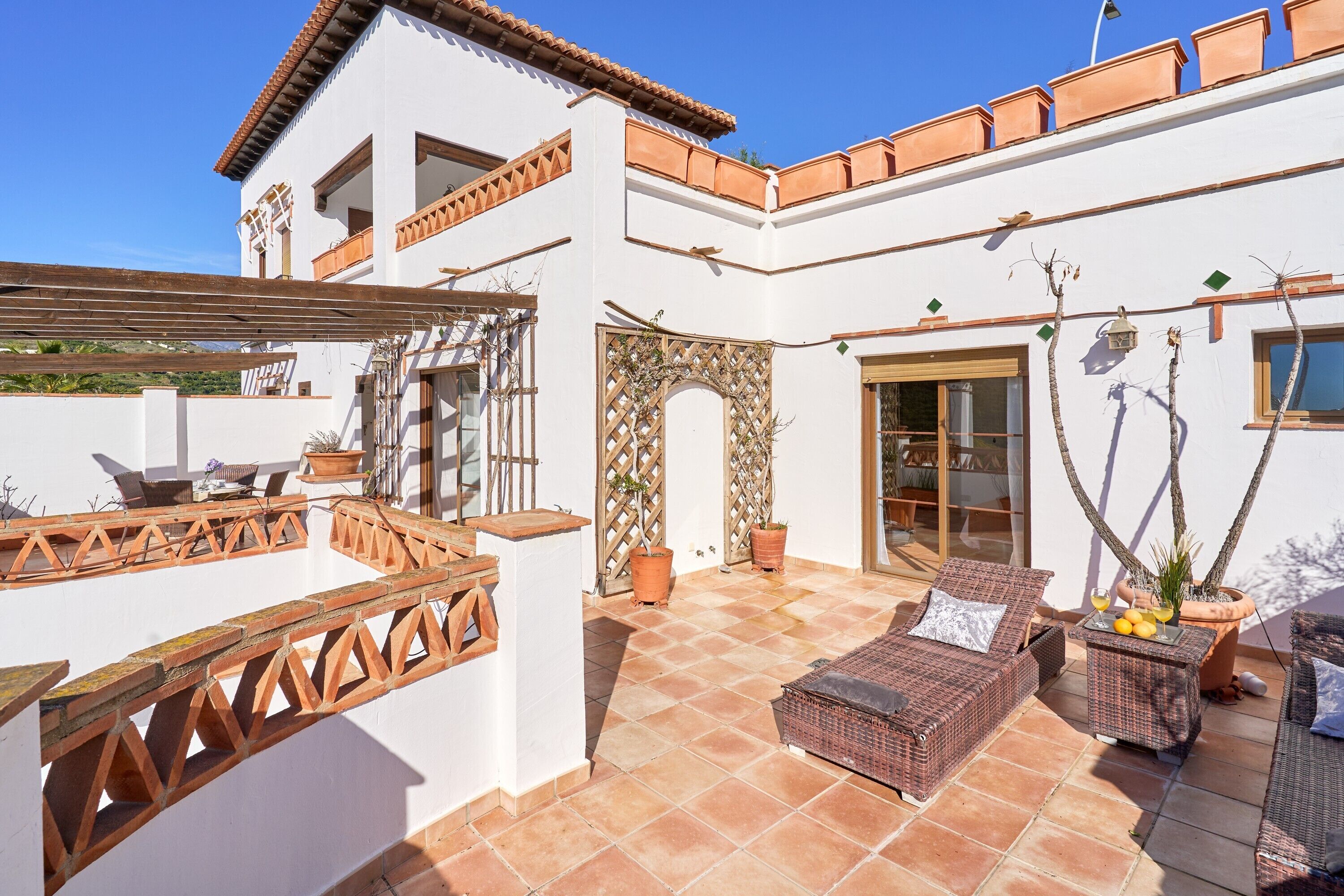 A patio with outdoor furniture, a pergola, and a white building with terracotta roof tiles.