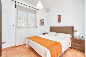 A bedroom with a bed, a nightstand, a lamp, a small plant, and a window with a curtain.