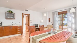A modern kitchen with wooden cabinets, a dining area with a wooden table and chairs, a TV, and a balcony with a view.