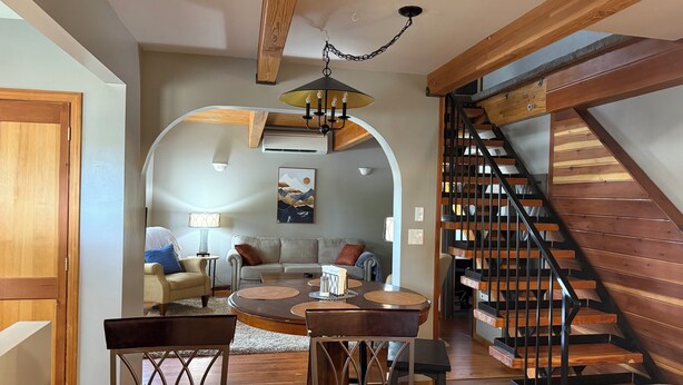 A spacious living area with a round coffee table, a sofa, and a dining table with chairs. A wooden staircase with a metal railing leads to an upper level. - Cozy 2+ bedroom house in beautiful Springfield (Springfield)