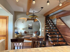 A spacious living area with a round coffee table, a sofa, and a dining table with chairs. A wooden staircase with a metal railing leads to an upper level. - Cozy 2+ bedroom house in beautiful Springfield (Springfield)