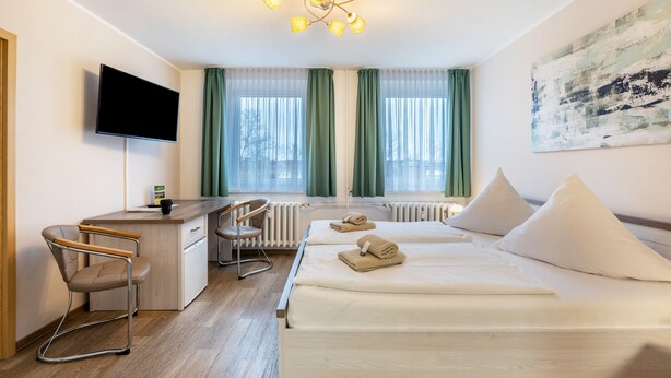 A hotel room with a bed, a desk, a chair, a TV, and a window with curtains. - Standard Double Room – Pension Clara Klipphausen (Klipphausen)