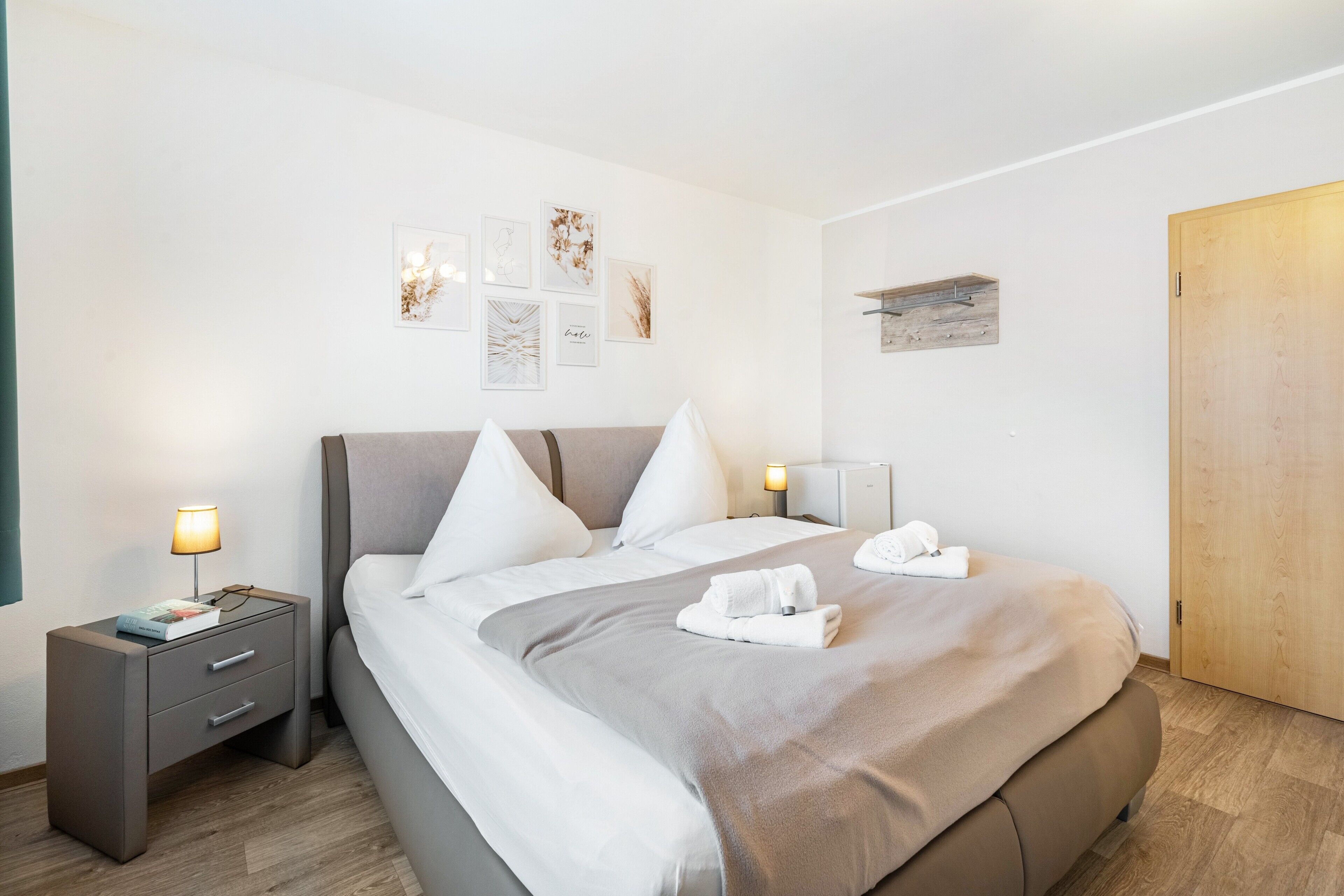 Una camera d'albergo ordinata con un letto, comodini, opere d'arte a parete e una porta in legno.