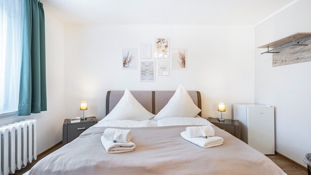 Un lit bien fait, avec des oreillers, une table de chevet avec une lampe, une étagère fixée au mur et un radiateur.