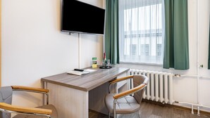 Une chambre d’hôtel équipée d’un téléviseur à écran plat, d’un bureau en bois, de deux chaises, d’un radiateur et d’une fenêtre avec des rideaux verts.