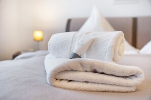 Une serviette blanche, soigneusement pliée, est posée sur un lit, avec un oreiller et une lampe de chevet en arrière-plan.